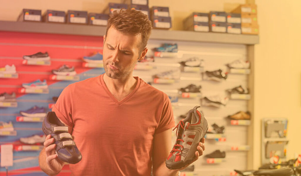 A man in a store holding two different pairs of running shoes, deciding which one to purchase.