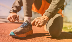 A man on a running track bending down to fix the laces of his worn-out shoes.